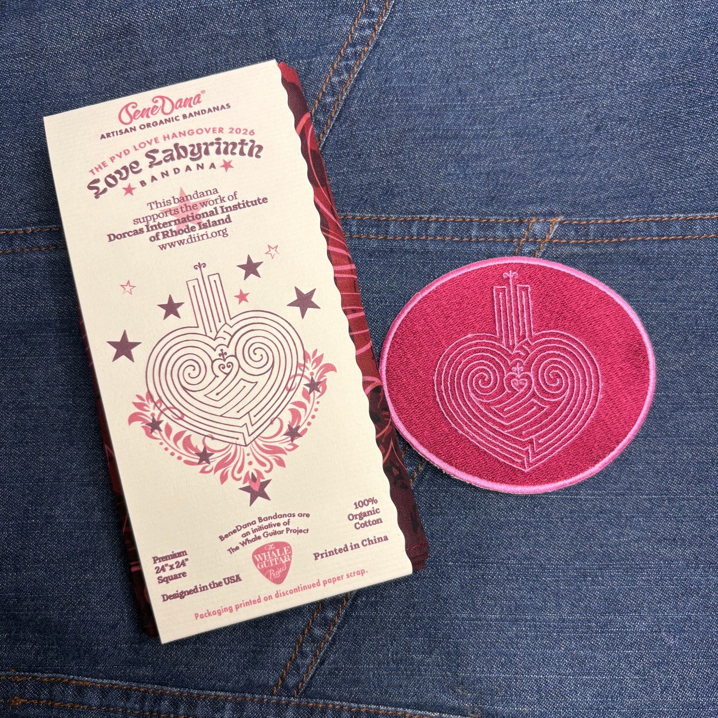 Pink circular patch and a packaged bandana with a Love Labyrinth design on a blue denim background